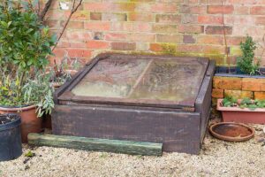 A horizontal image of a cold frame with the lid closed, set outside a brick structure.