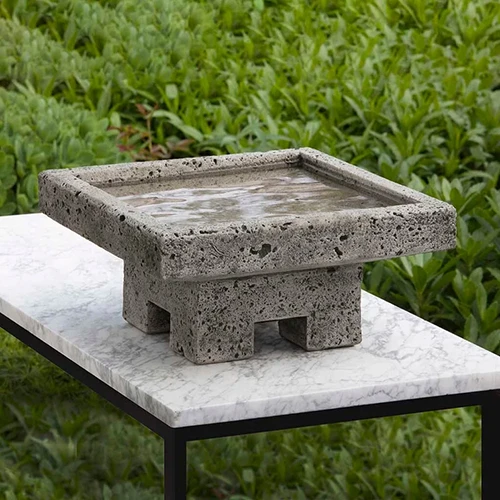 A close up square image of the Campania International Kosei birdbath set on a marble table outdoors.