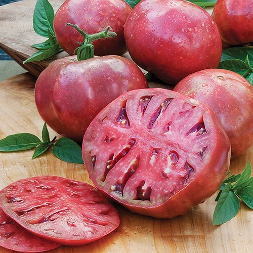 A close up of whole and sliced 'Cherokee Purple' tomatoes set on a wooden surface.
