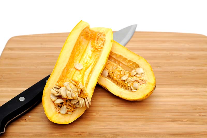 A close up horizontal image of a 'Delicata' squash sliced in half with the seeds scraped out set on a wooden chopping board.