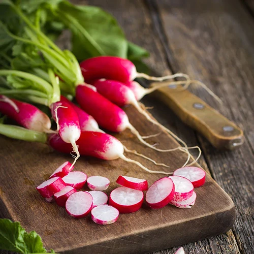 A square image of 'Fresh Breakfast' radishes, whole and sliced, set on a wooden chopping board.