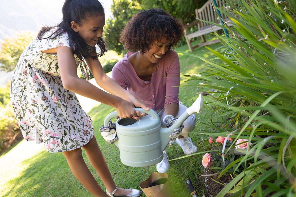 A close up horizontal image of a mother and her daughter watering flowers in the garden.
