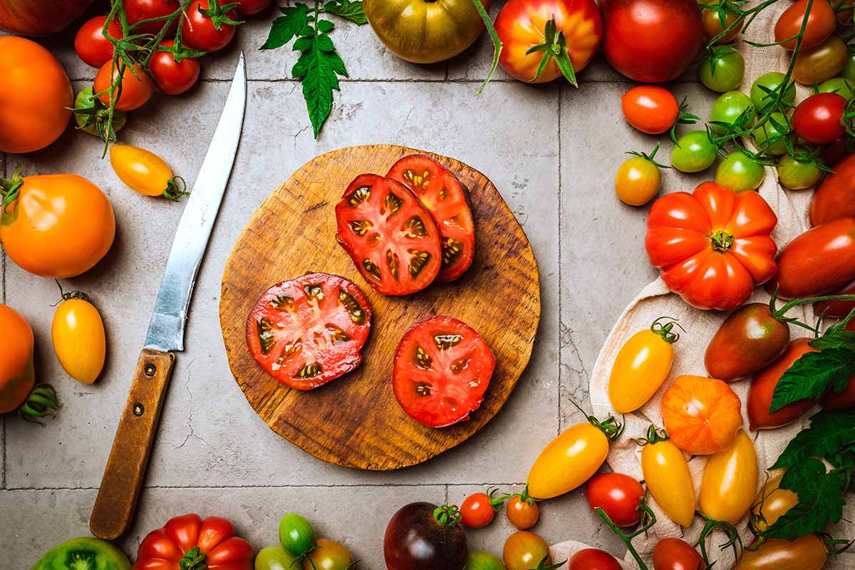 A close up horizontal image of a wide variety of different tomatoes, both sliced and whole, in different colors and sizes.