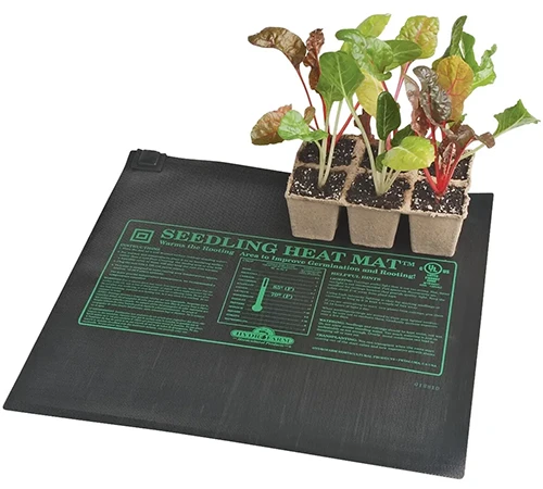 A close up of a heat mat with a small tray of seedlings resting on it pictured on a white background.