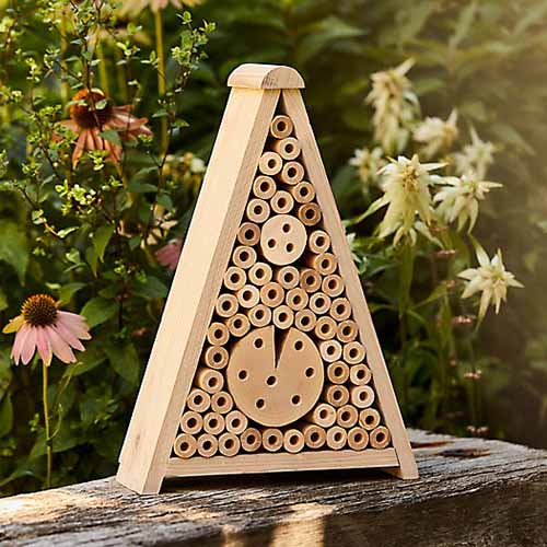 A close up square image of a triangle insect hotel set on a wooden surface.