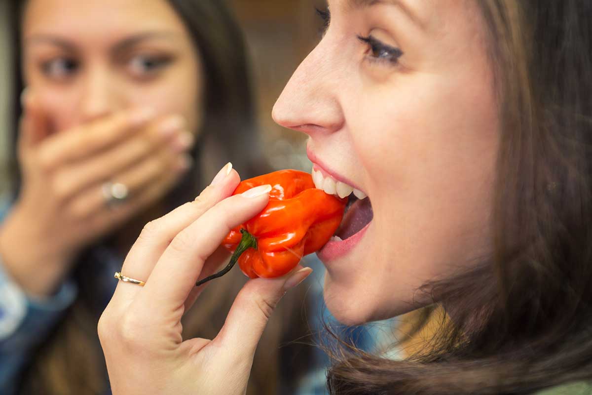 A close up horizontal image of a woman biting into a habanero pepper.