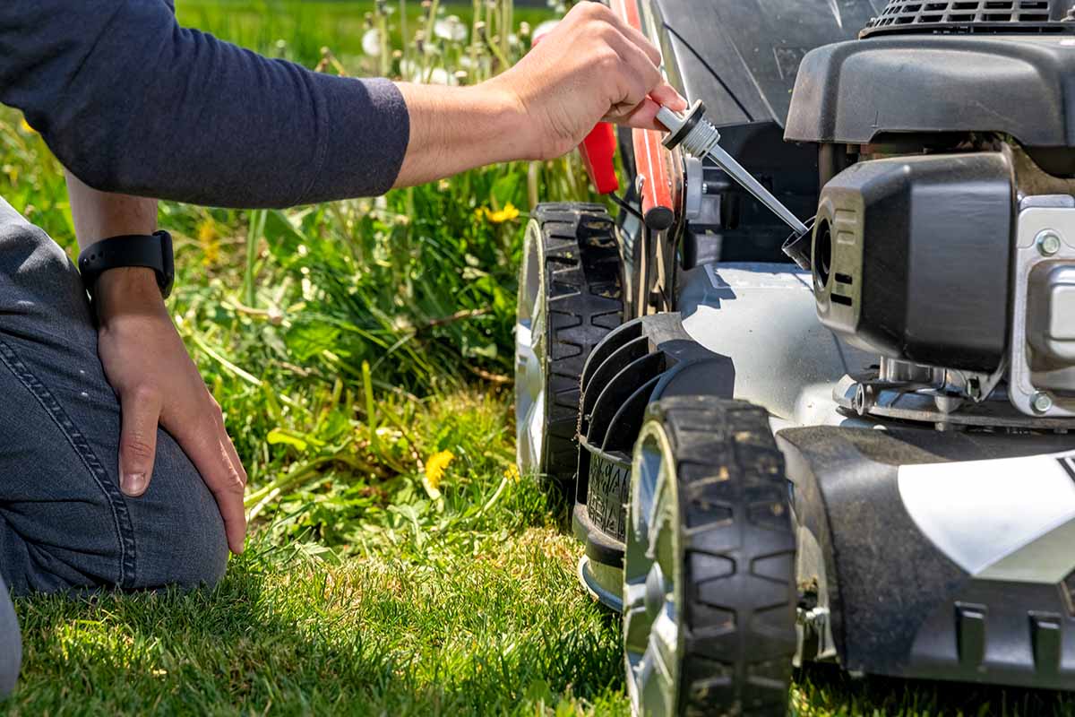 A close up horizontal image of a gardener checking the oil in a gas mower.