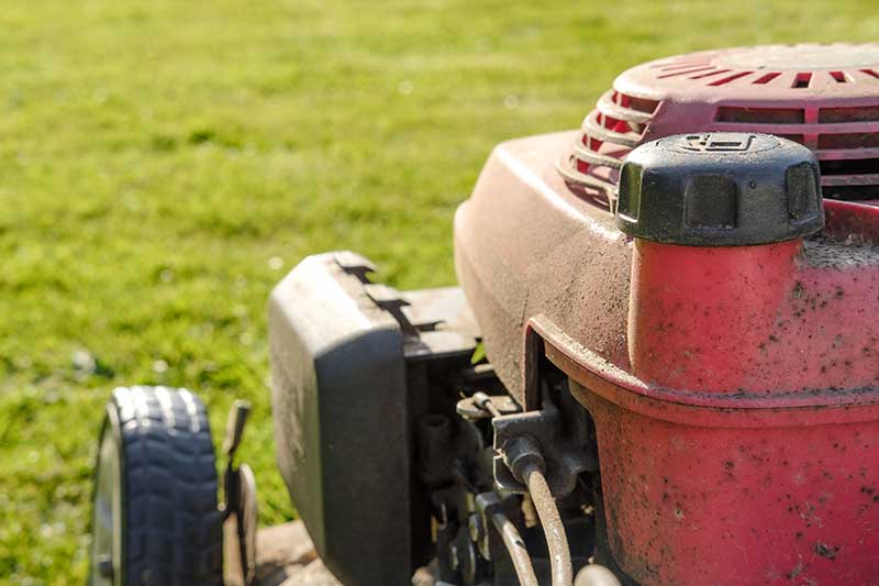 A close up horizontal image of a the engine of a gas lawn mower.