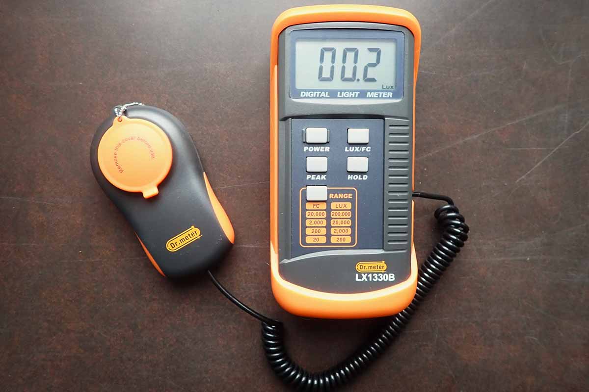 A close up horizontal image of a black and orange light meter set on a dark surface.