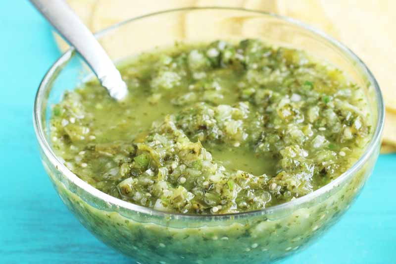 A close up of a bowl of freshly prepared salsa verde set on a blue surface.