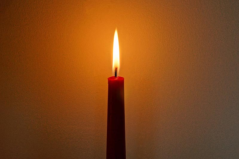 A close up horizontal image of a single burning candle on a soft focus background.
