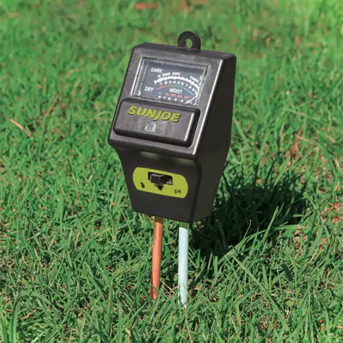 A close up square image of a soil moisture meter stuck into a lawn.