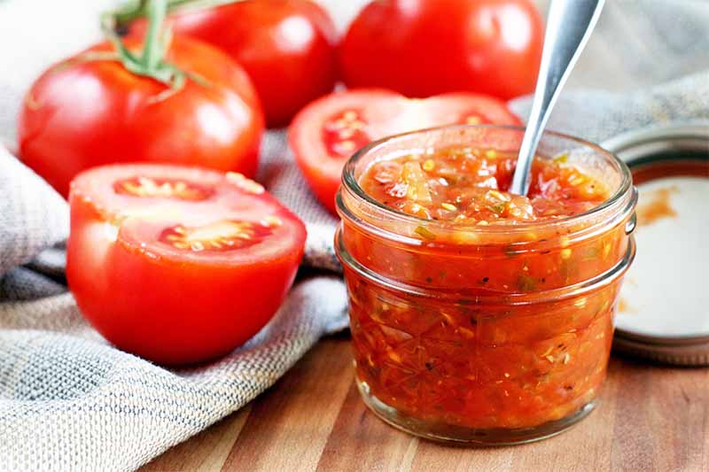A close up horizontal image of fresh homemade tomato jam in a jar set on a wooden surface.