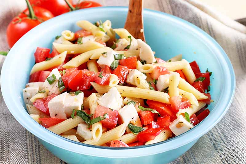 A close up horizontal image of a freshly-prepared pasta salad in a blue bowl.