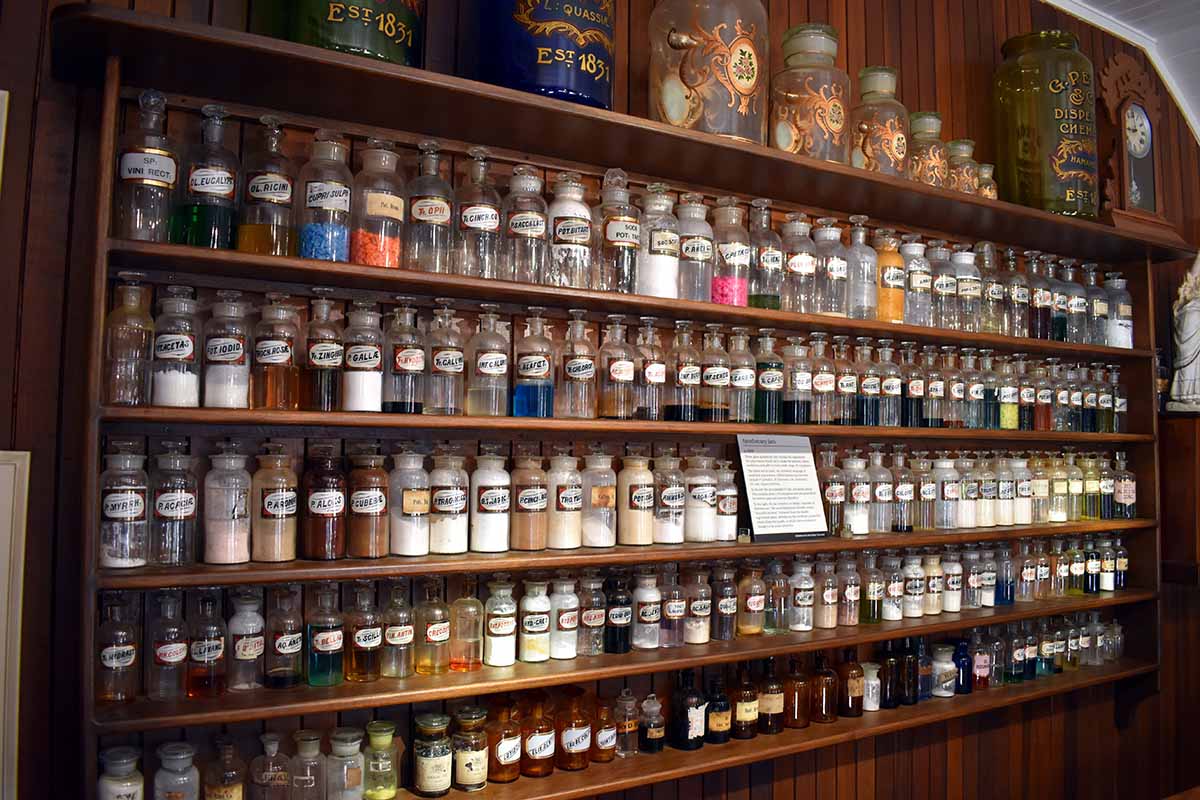 A horizontal image of indoor wooden shelves containing glass jars filled with various herbal medicines.