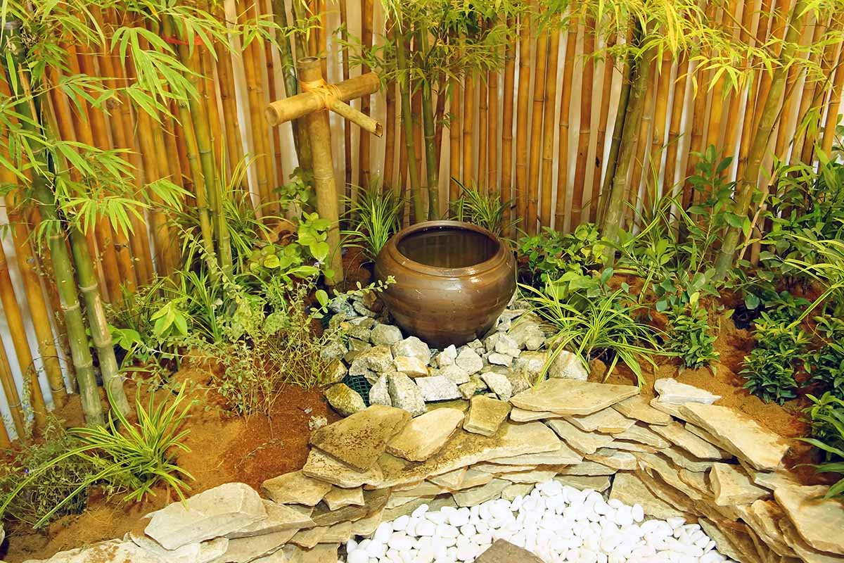 A close up horizontal image of a zen garden featuring bamboo, decorative stones, and a water feature.