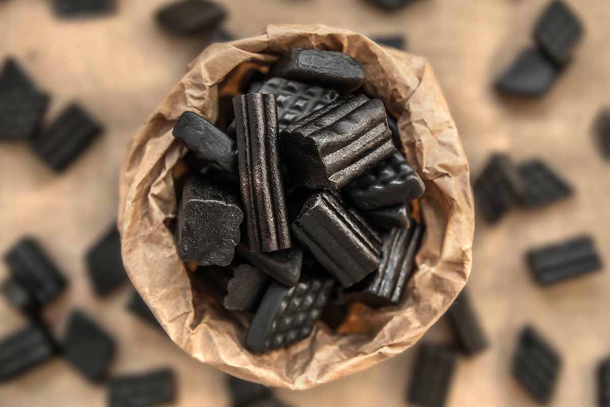 A close up horizontal image of black licorice in a small pot.