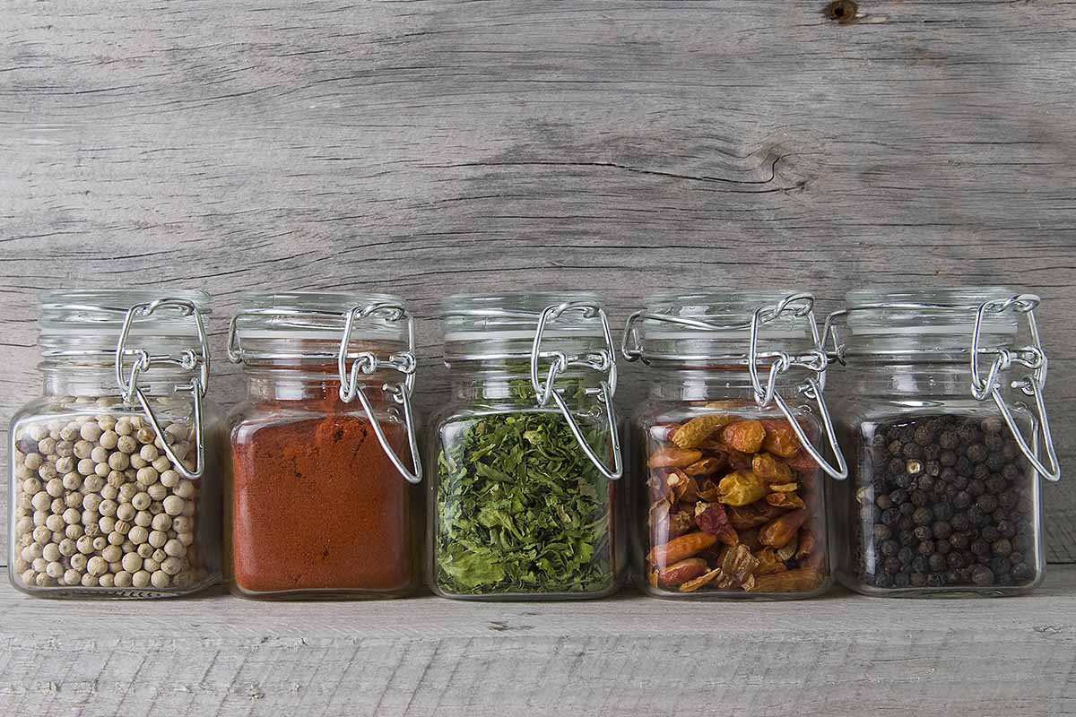A close up of jars of dried herbs set on a wooden surface.