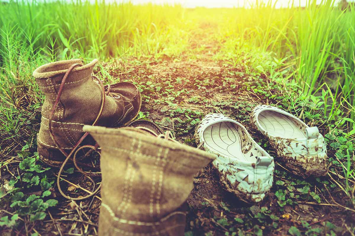 A close up horizontal image of two pairs of shoes set on the ground in the garden.