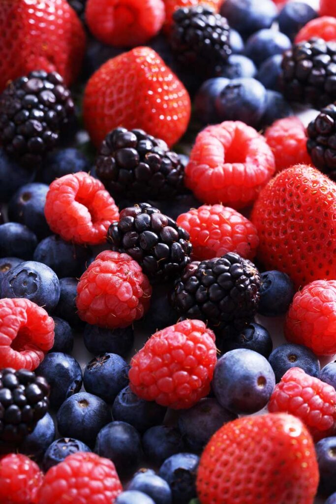 A mixture of small berries with bright colors resting in a pile. There are blueberries, blackberries, strawberries and raspberries in the fruit assortment.