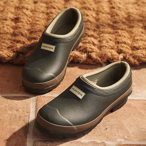 A close up of the Hunter Women's Gardener Clog in dark olive/clay set on a brick surface.
