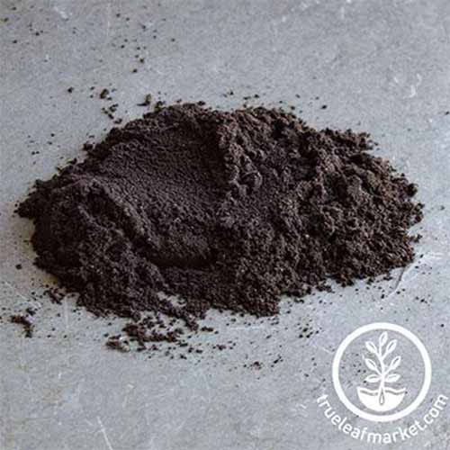 A square image of a pile of powdered inoculant set on a light gray surface. To the bottom right of the frame is a white circular logo with text.