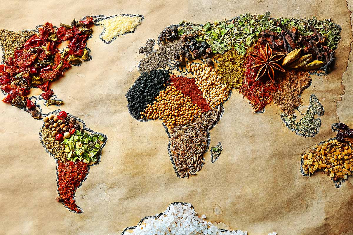 A horizontal image of a world map on brown paper, with various regions illustrated with different spices.