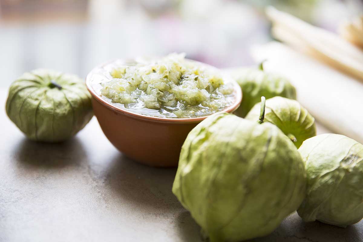 A close up horizontal image of freshly prepared salsa verde with ripe tomatillos scattered around.