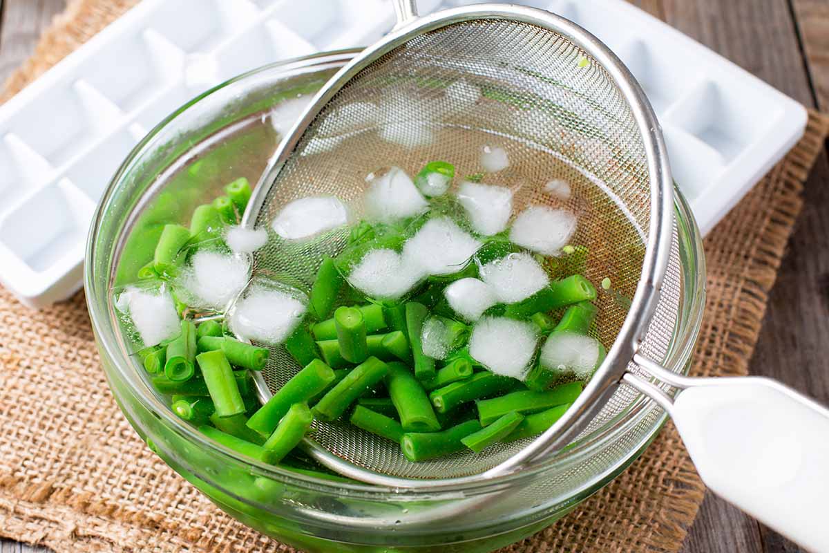 A horizontal image of slices of green beans placed in a bowl of iced water.