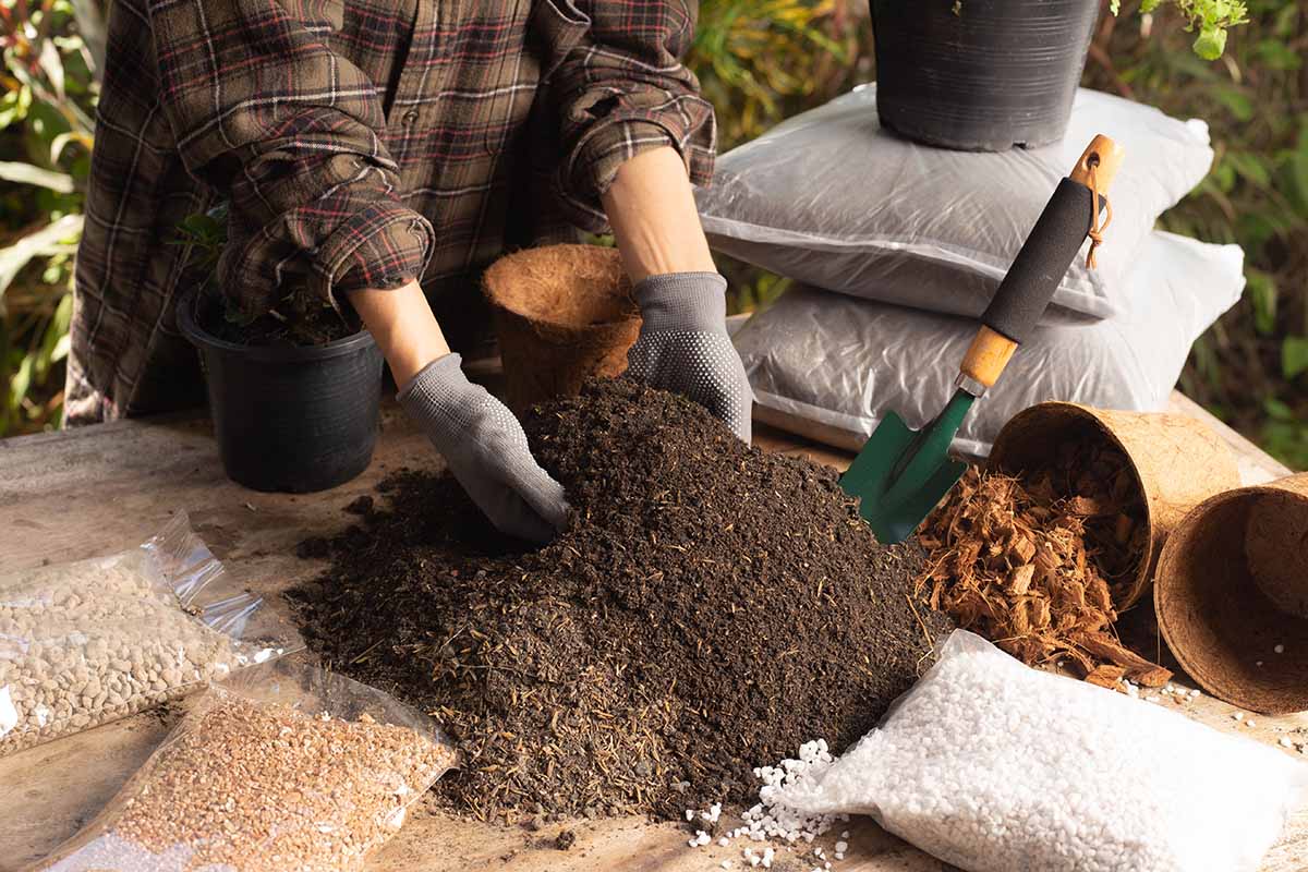 A horizontal image of a gardener mixing up potting soil for growing in containers.