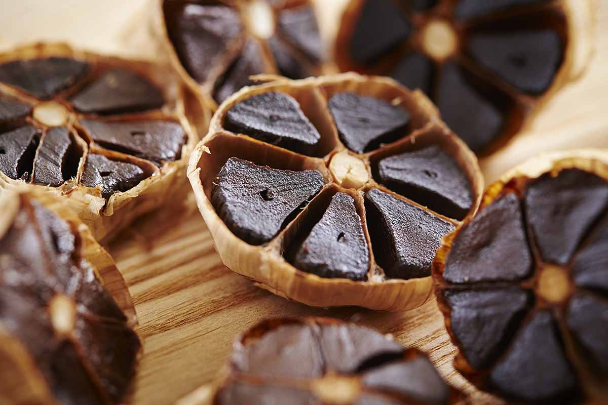 A close up horizontal image of black garlic bulbs cut in half to reveal the cloves inside.