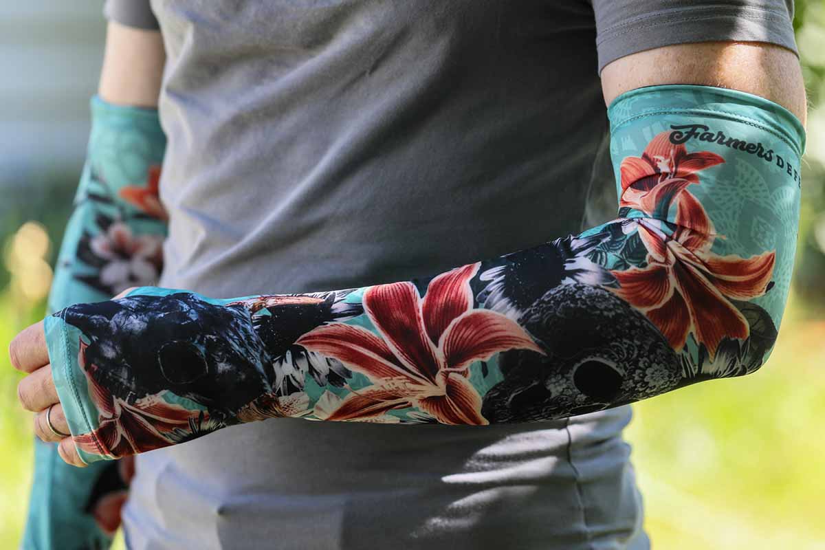 A close up horizontal image of a man wearing a Farmers Defense Sleeve decorated with flowers and skulls.