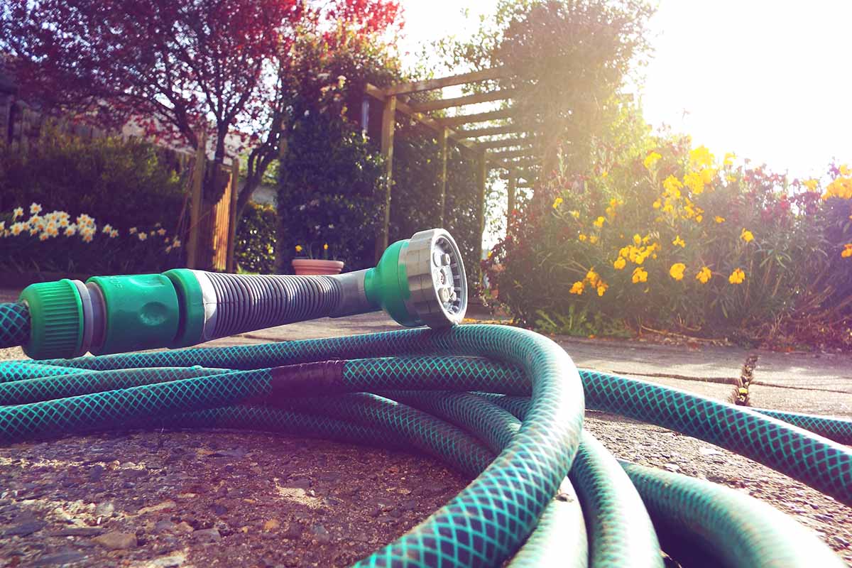 A close up horizontal image of a garden hose coiled on a patio pictured in evening sunshine.