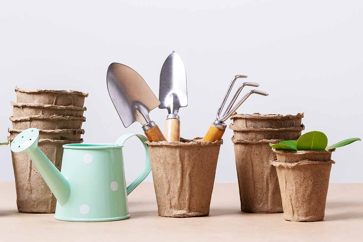 A close up horizontal image of recycled paper pots with tools and a watering can.