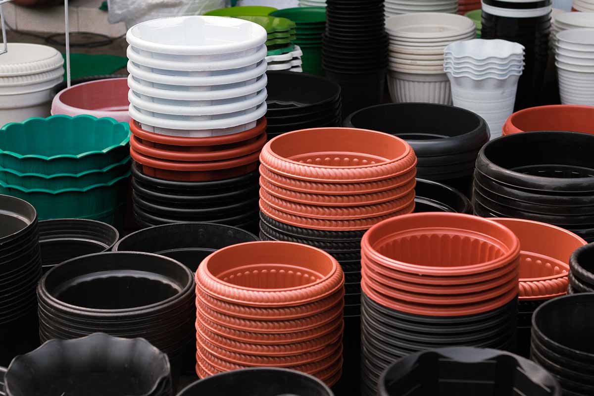 A horizontal image of a collection of different colored plastic pots stacked at a plant nursery.