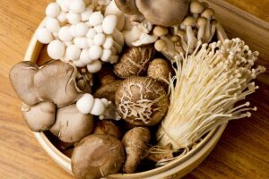 A close up horizontal image of a bowl filled with different kinds of mushrooms set on a wooden surface.
