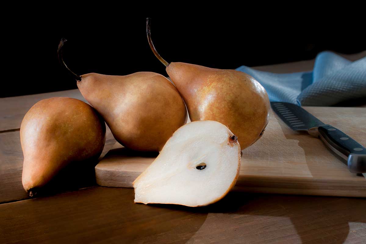A close up horizontal image of Bosc pears on a wooden chopping board with a knife.