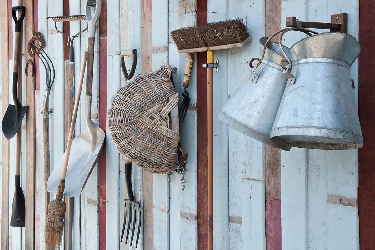 A close up horizontal image of a selection of gardening tools hung up neatly on a wall.