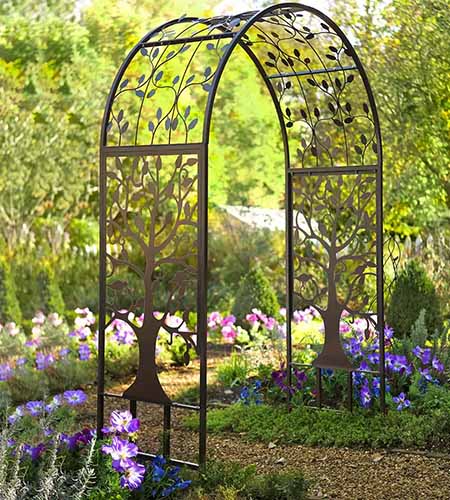 A close up of a metal arched garden arbor with a tree of life motif in the garden over a pathway.