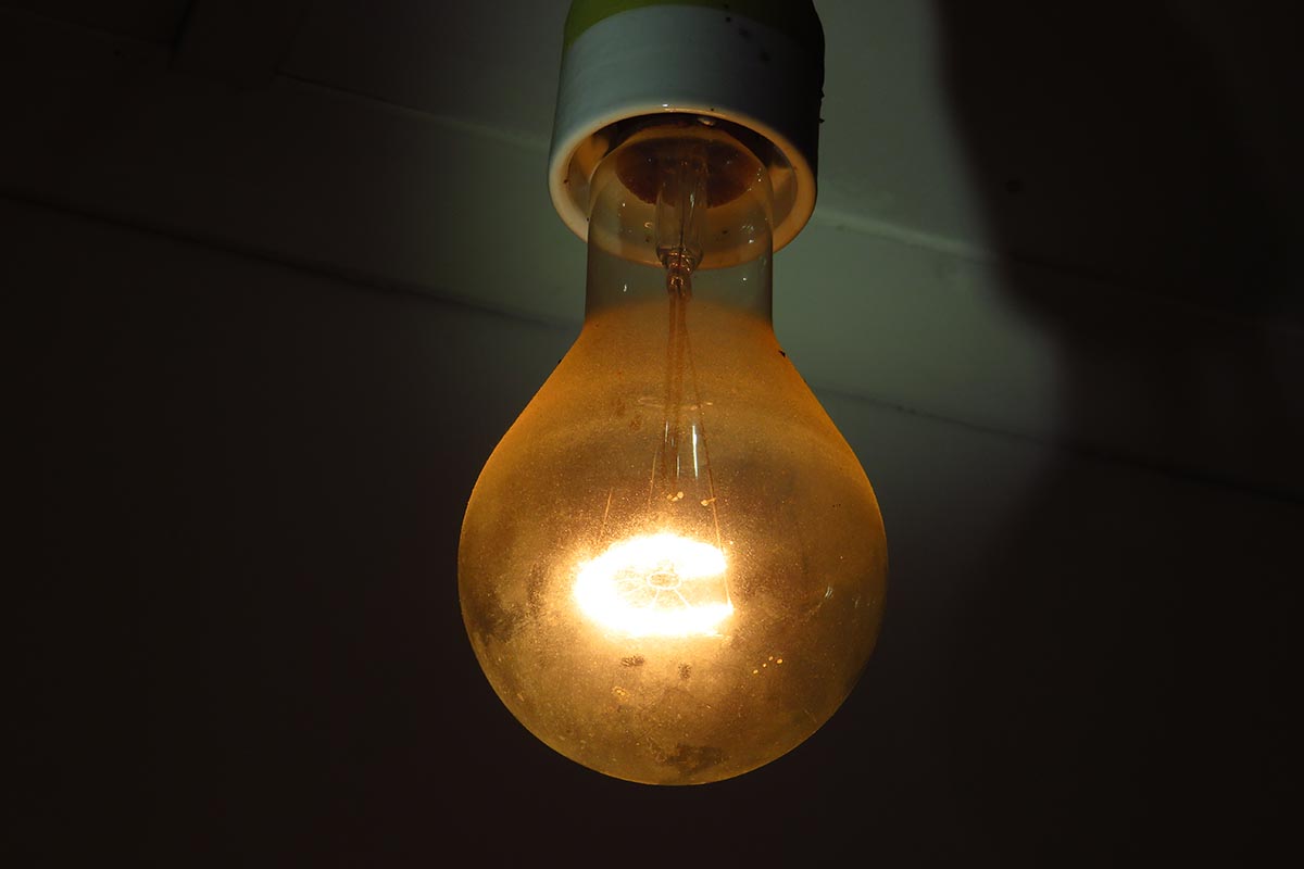 A close up horizontal image of an old dirty incandescent bulb illuminating a dark room.