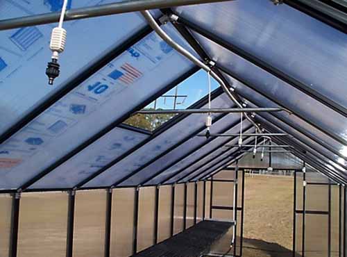 A horizontal shot of the roof of a greenhouse lined with an automatic watering system along the center ceiling.