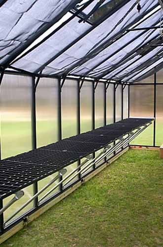 A vertical shot of one side of a greenhouse with a work bench system running along the entire length of the greenhouse.