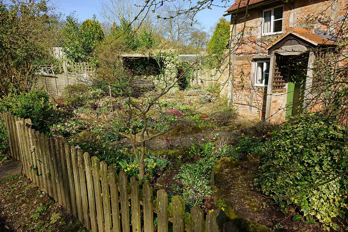A horizontal image of a brick home in the countryside with a cottage garden planted out front.