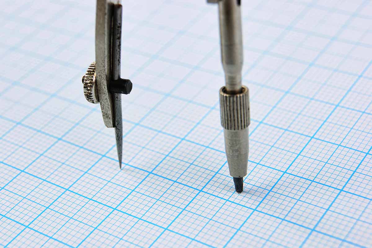 A close up horizontal image of a piece of graph paper with a drawing compass.