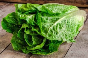 A horizontal shot of a head of lettuce on a wooden table. White spots are visible on the leaves of the lettuce.