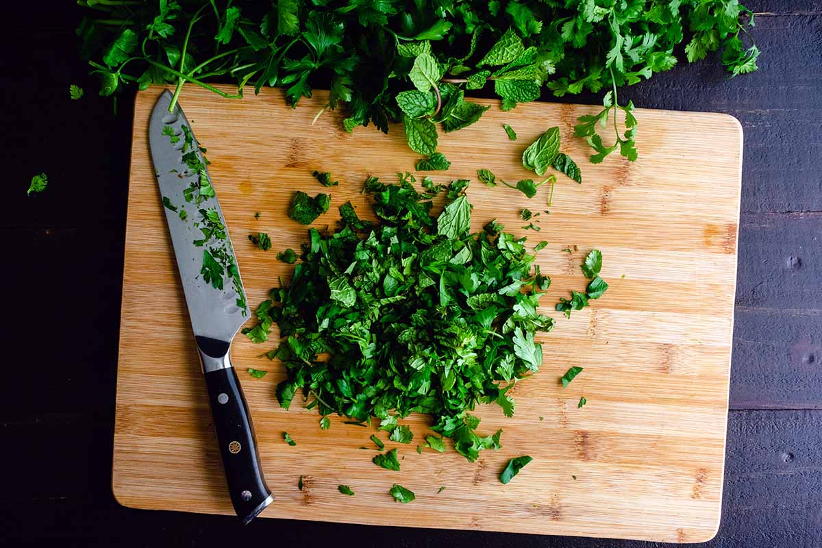 A close up horizontal image of a bamboo chopping board with mint and a knife, set on a dark wooden surface.