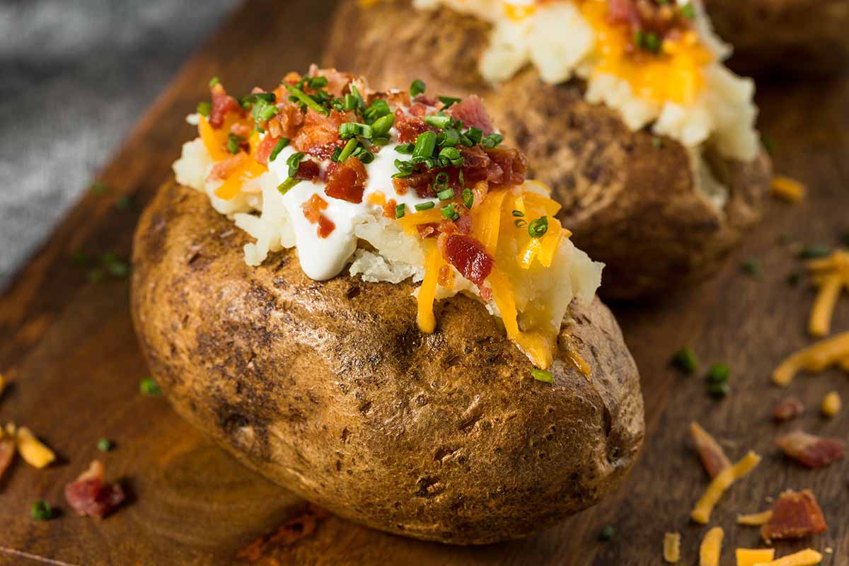 A horizontal photo of a "loaded" baked potato with sour cream, shredded cheese, bacon bits and green onion.