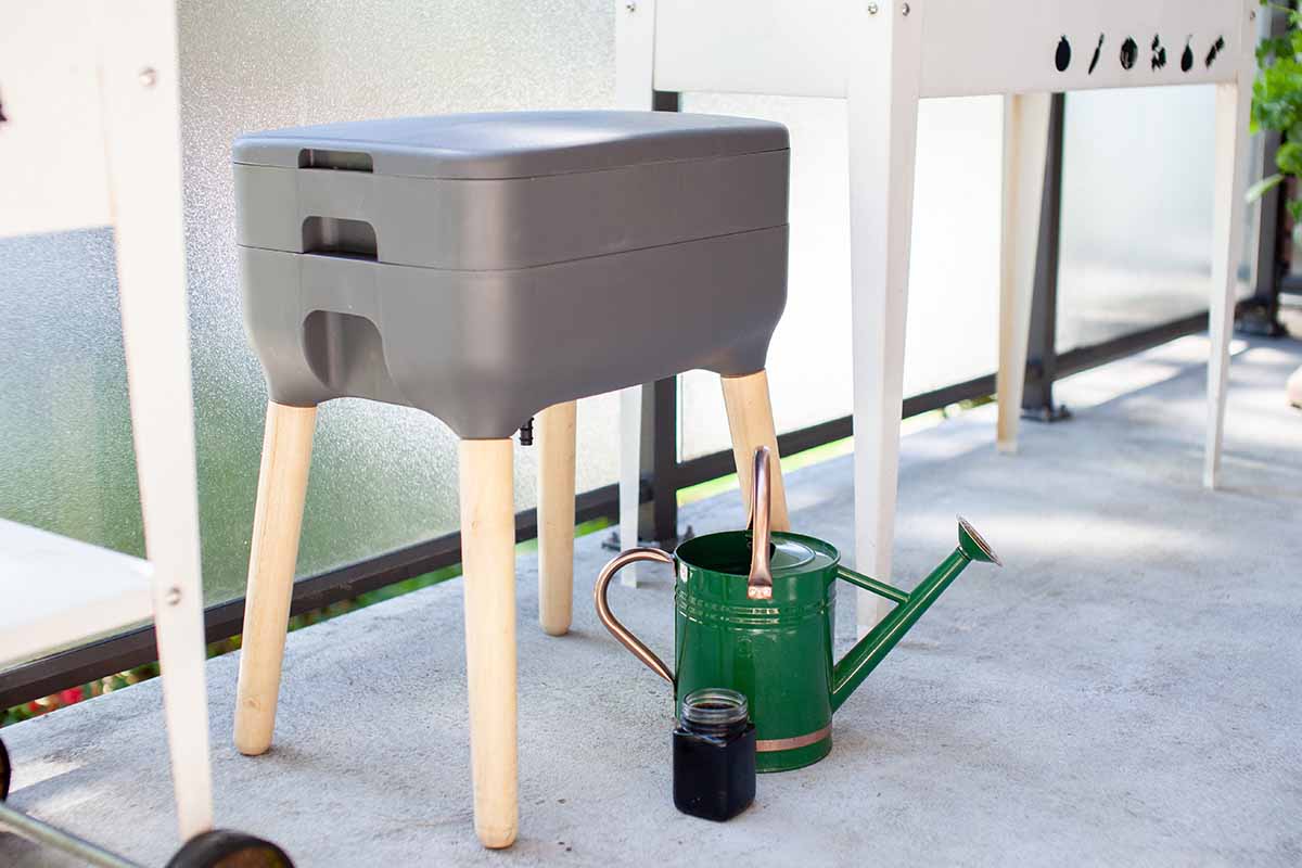 A horizontal shot of a vermicompost bin on wooden legs with a green metal watering can.
