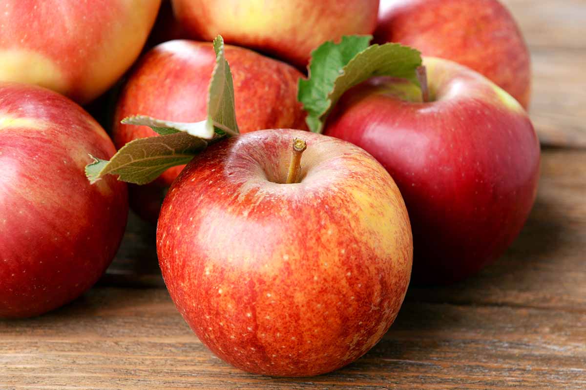 A close up horizontal image of apples set on a wooden surface.