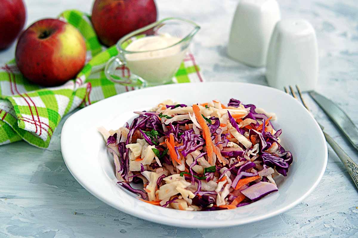 A close up horizontal image of a plate of freshly made coleslaw on a blue table.